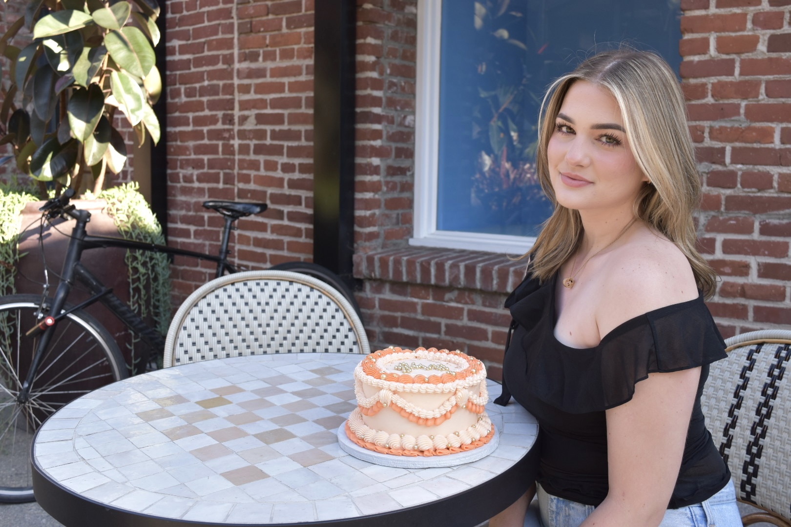 Sara sitting beside a cake for the fifth anniversary of Etched and Elegant